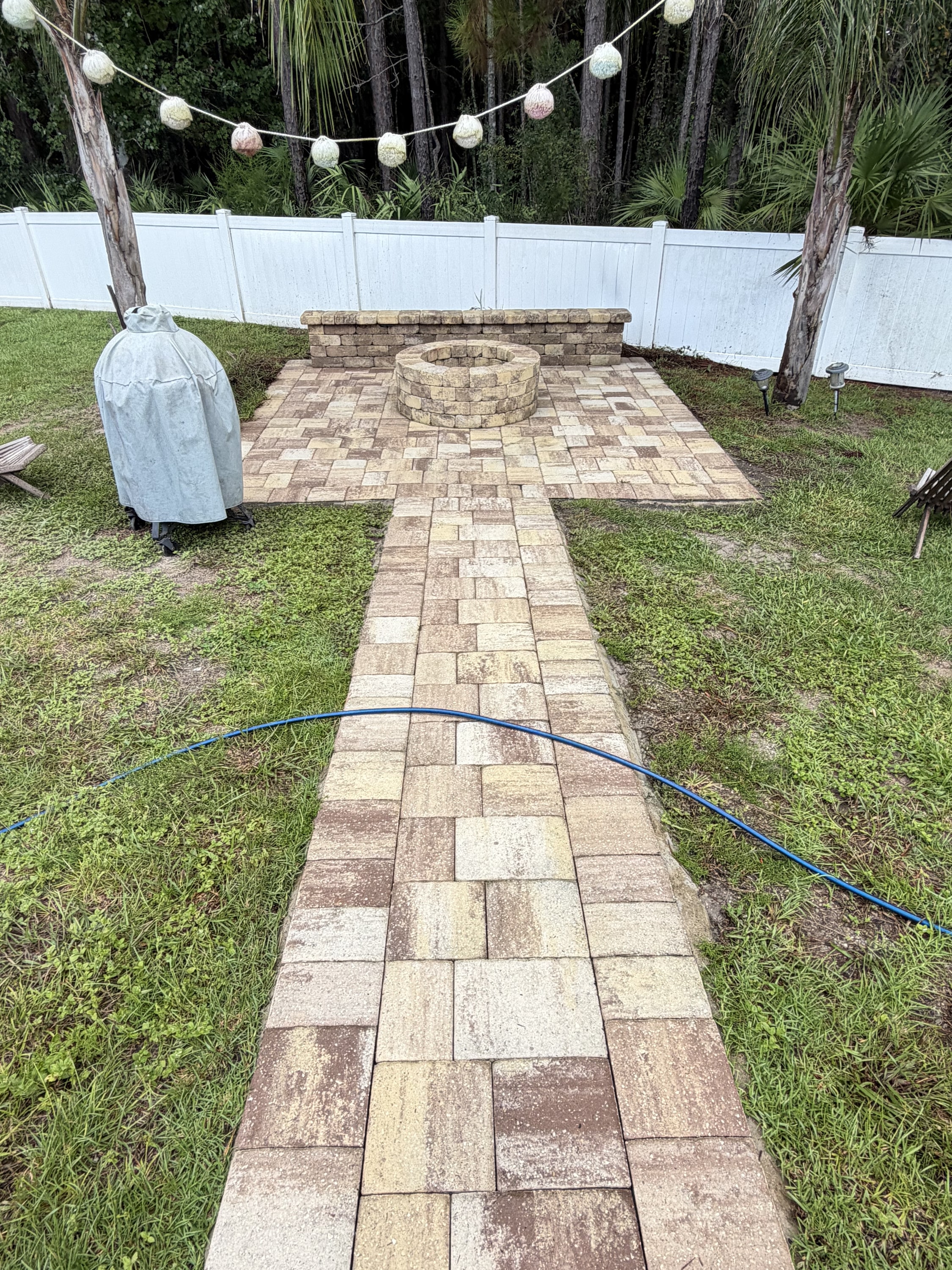 Paver patio with circular fire pit, seating wall, and string lights in a fenced garden