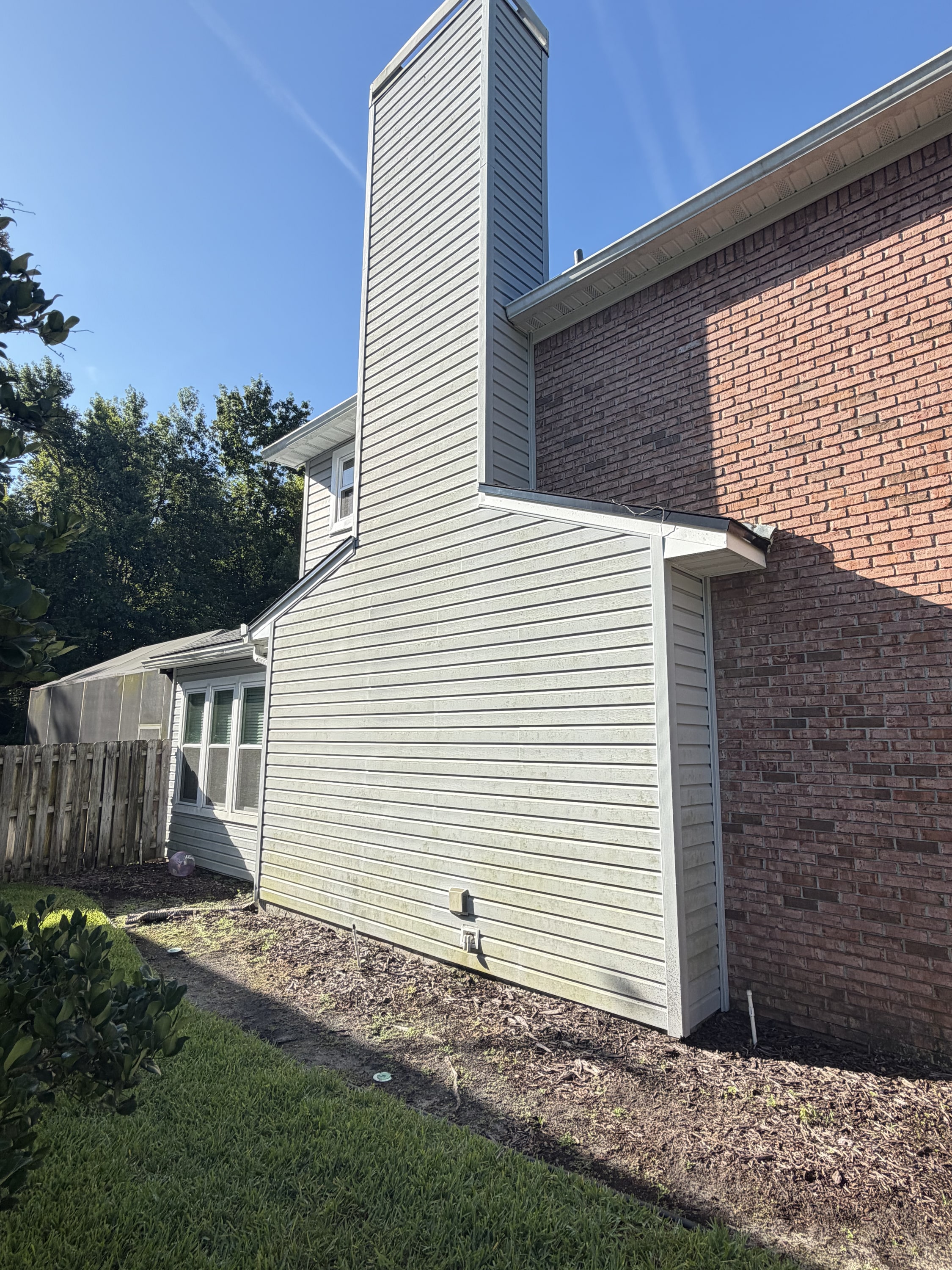 White vinyl siding on house extension with brick chimney and new roof against blue sky.