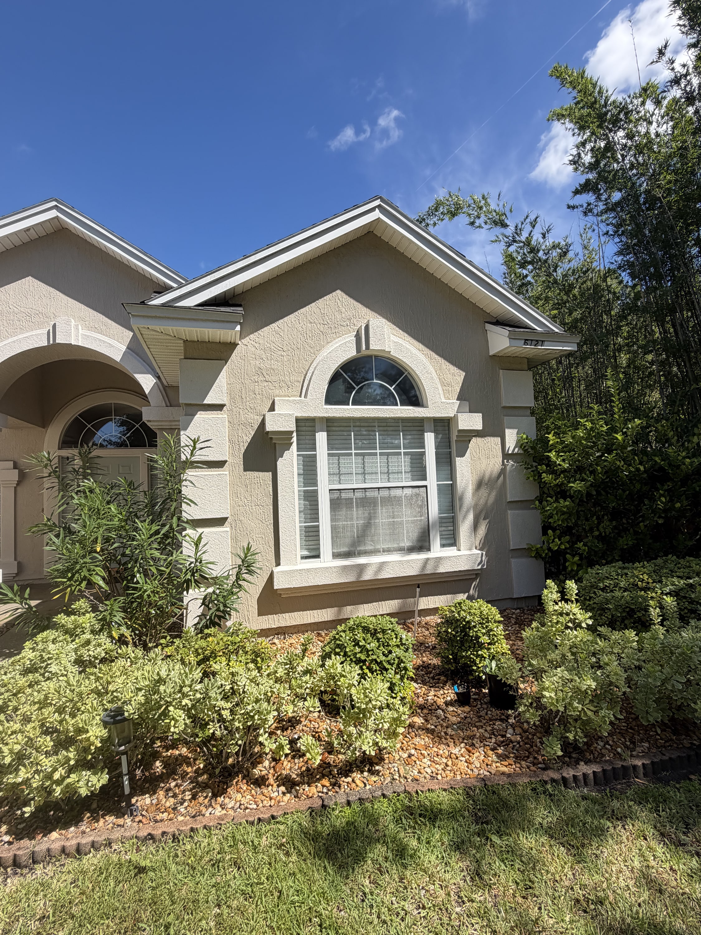 Cream rendered house front with white-trimmed arched windows and guttering in daylight.