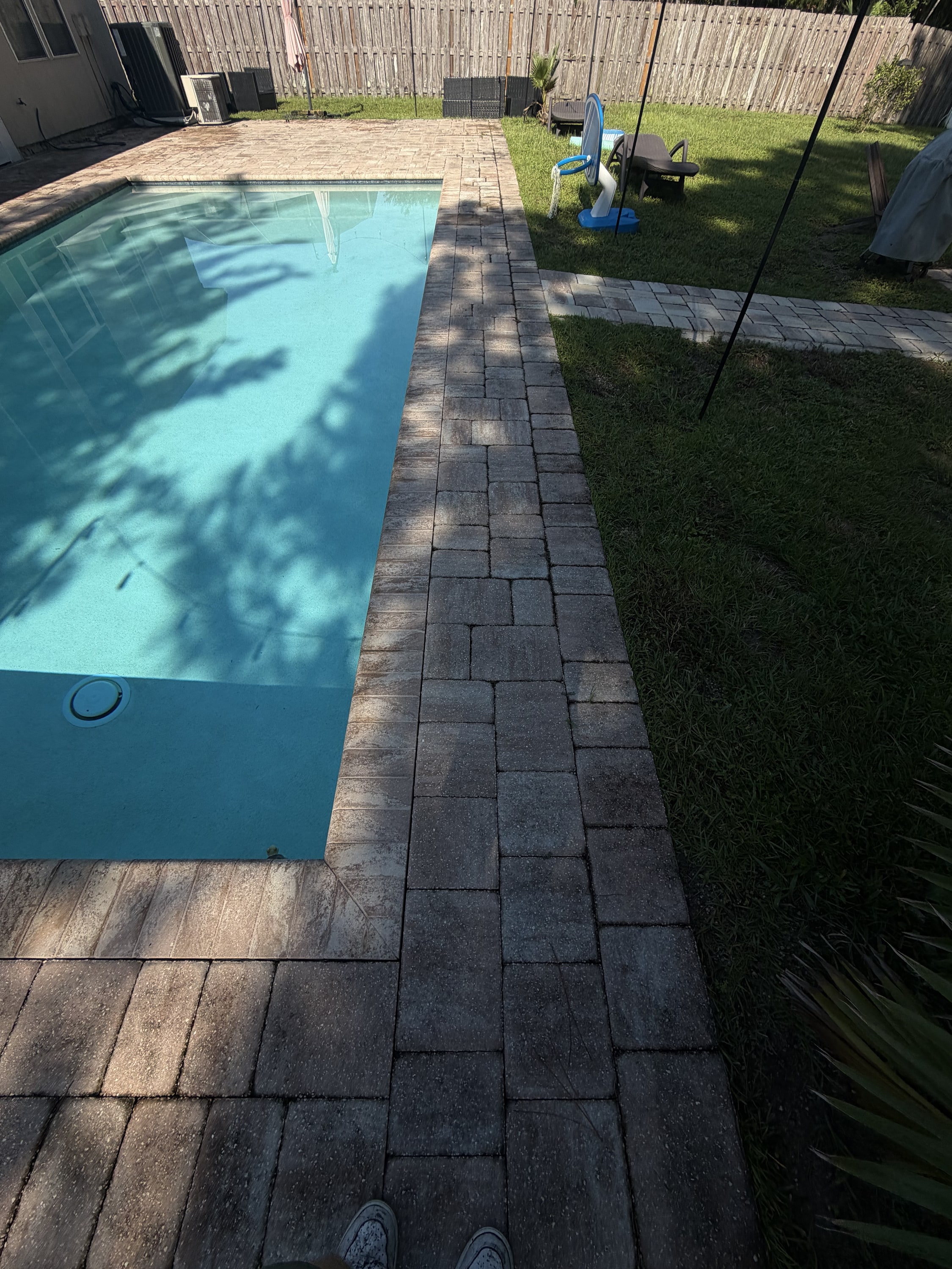 Completed dark paver pool deck and patio installation around a turquoise swimming pool