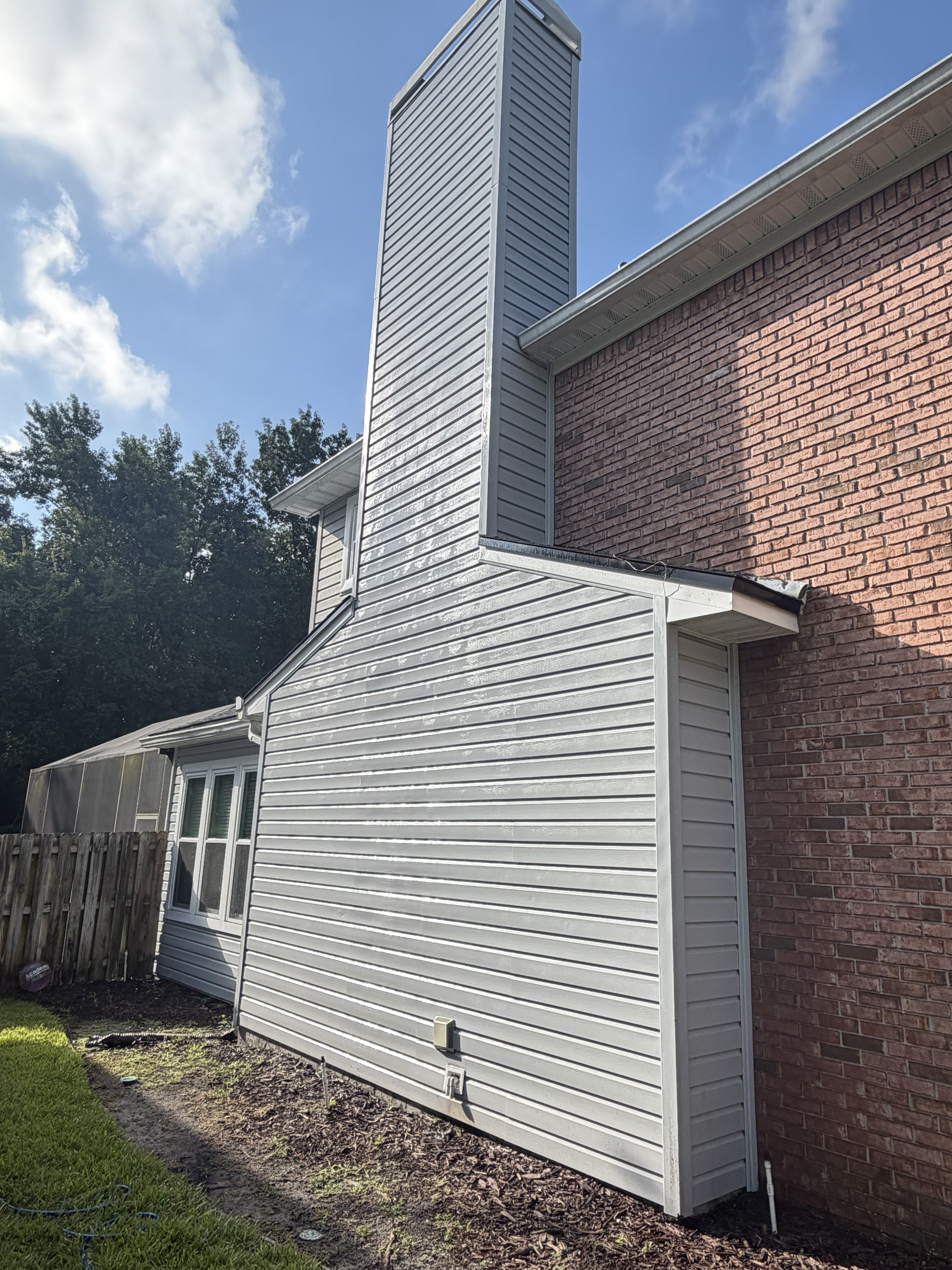 Grey vinyl-clad two-storey house extension with chimney, attached to brick building.