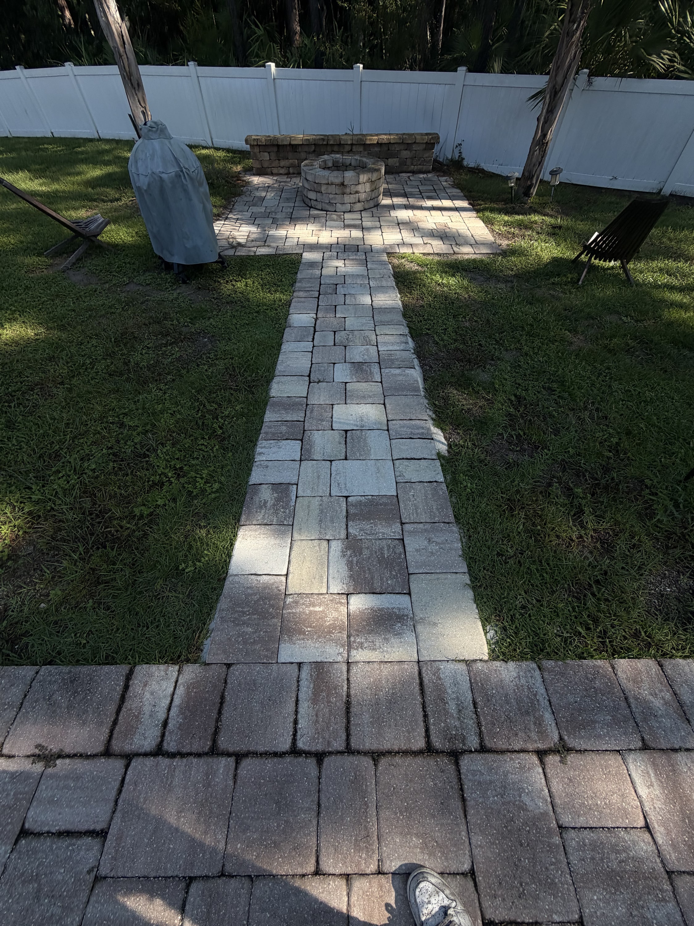 Block paved pathway with circular fire pit in completed garden with white vinyl fencing.
