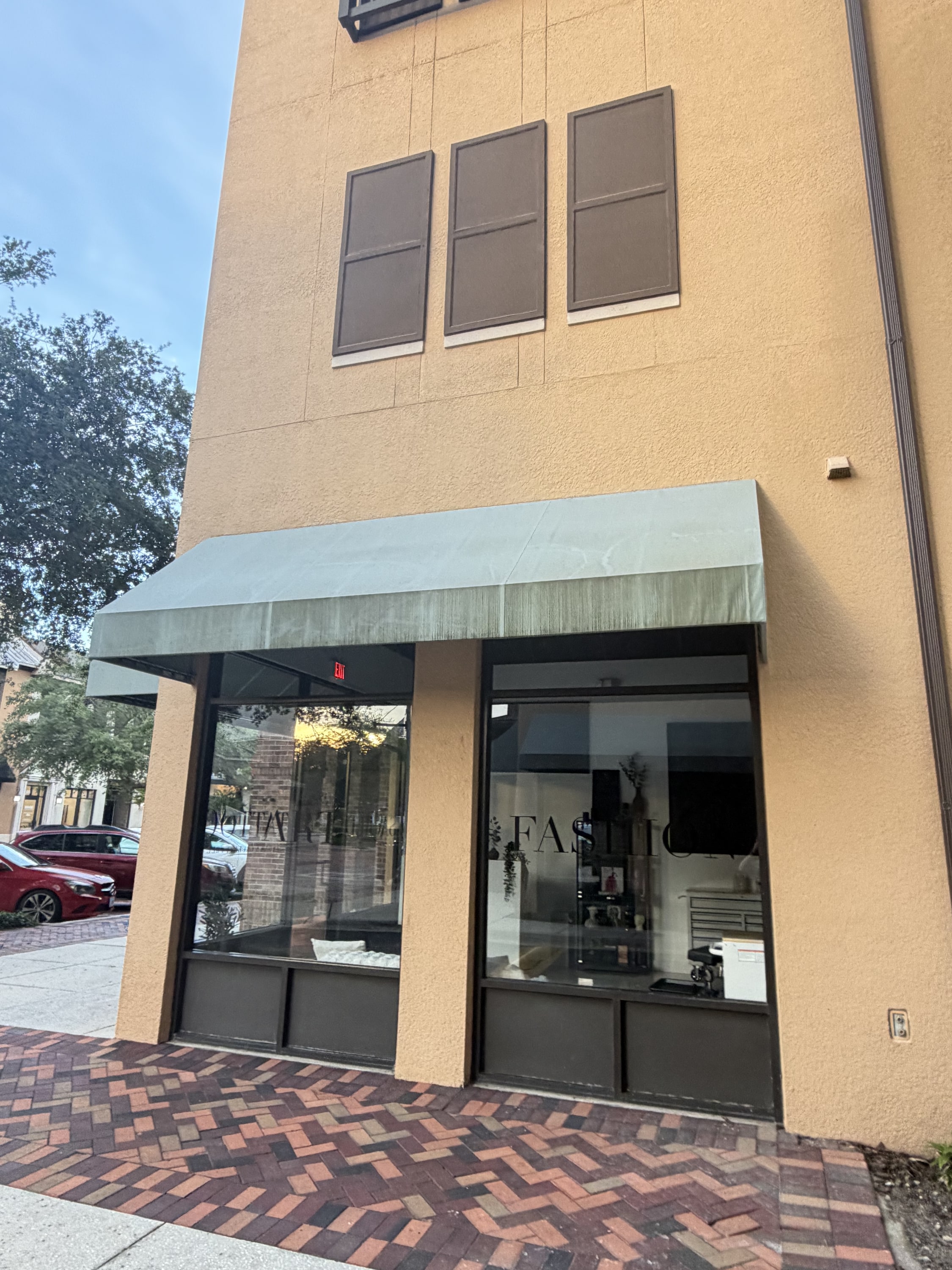 Retail storefront with grey metal awning, dark-framed windows, and herringbone brick paving.