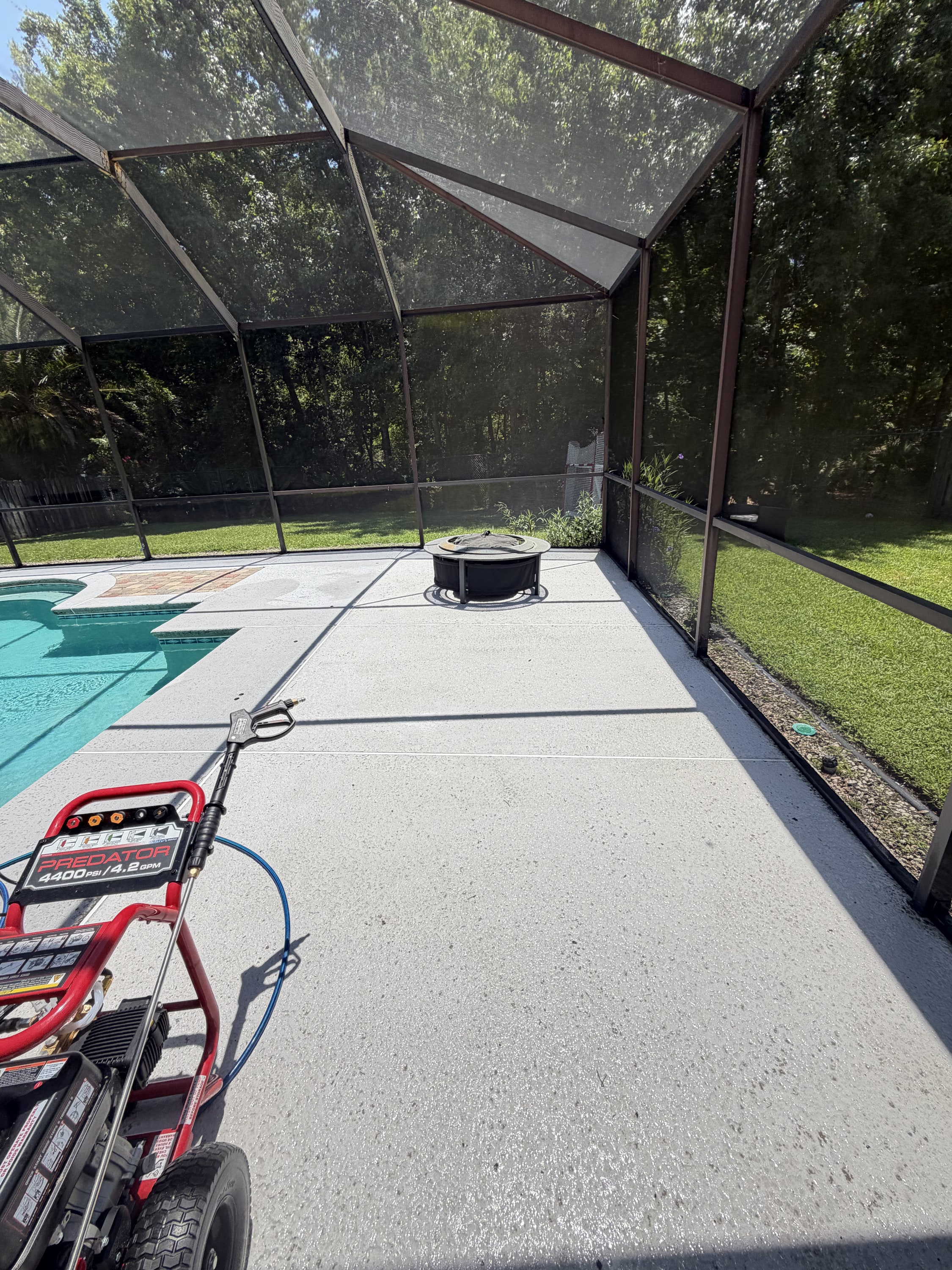 Pressure washer on concrete patio inside screened enclosure with pool visible.