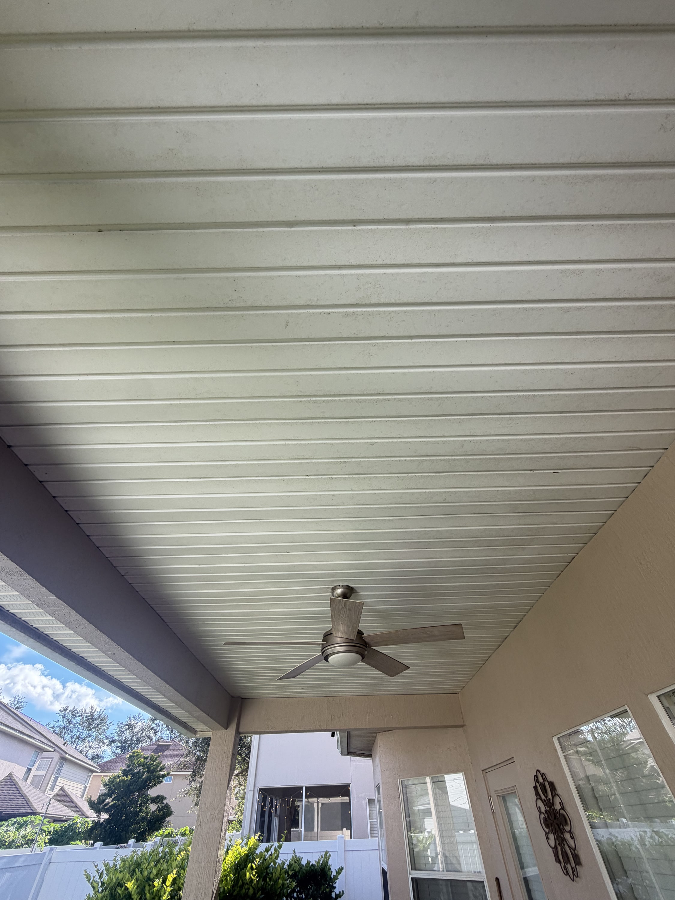 White slatted aluminium ceiling with ceiling fan installed in a covered patio area.