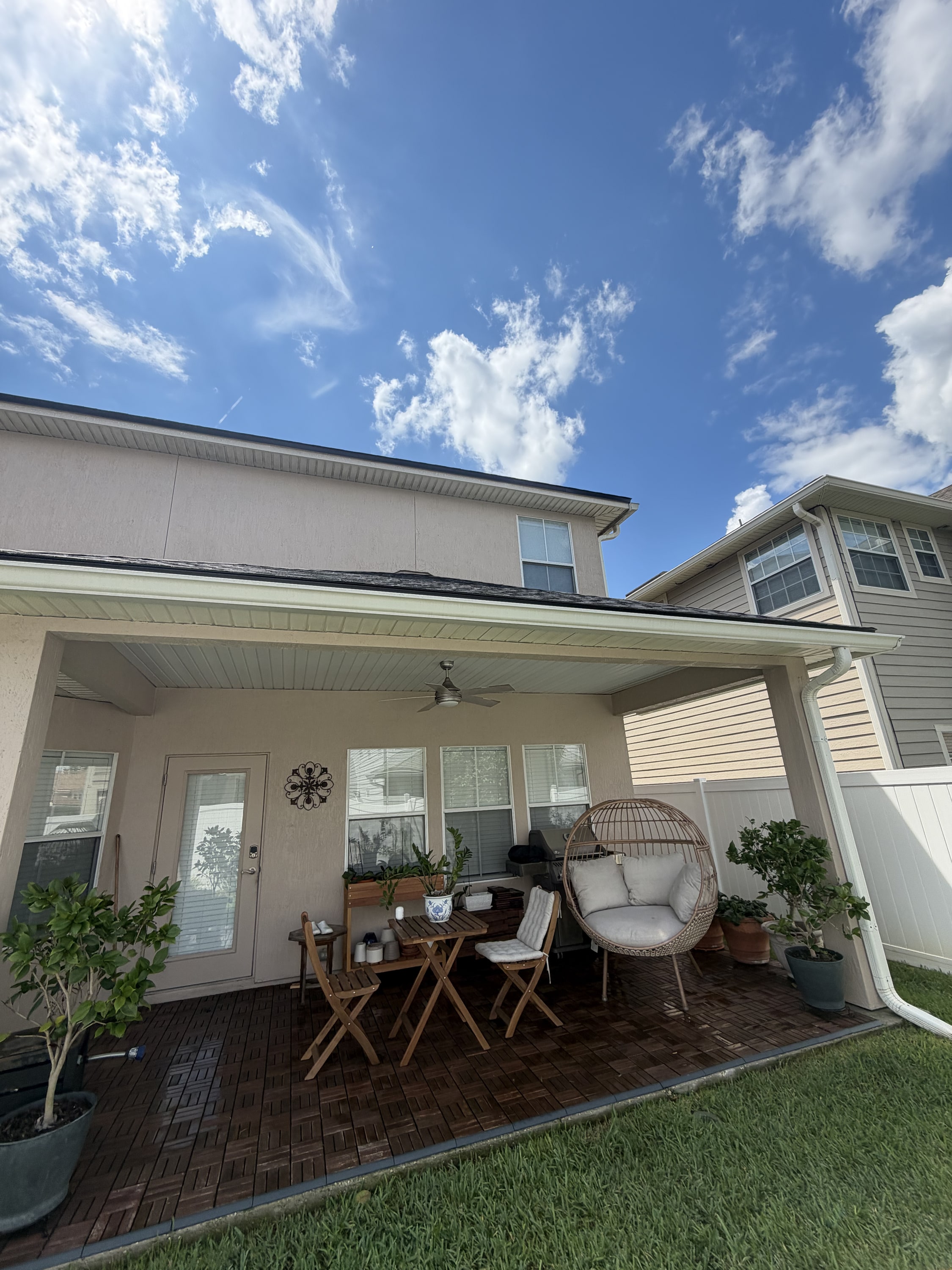 Covered patio with composite deck, white ceiling and ceiling fan, furnished with chairs and plants