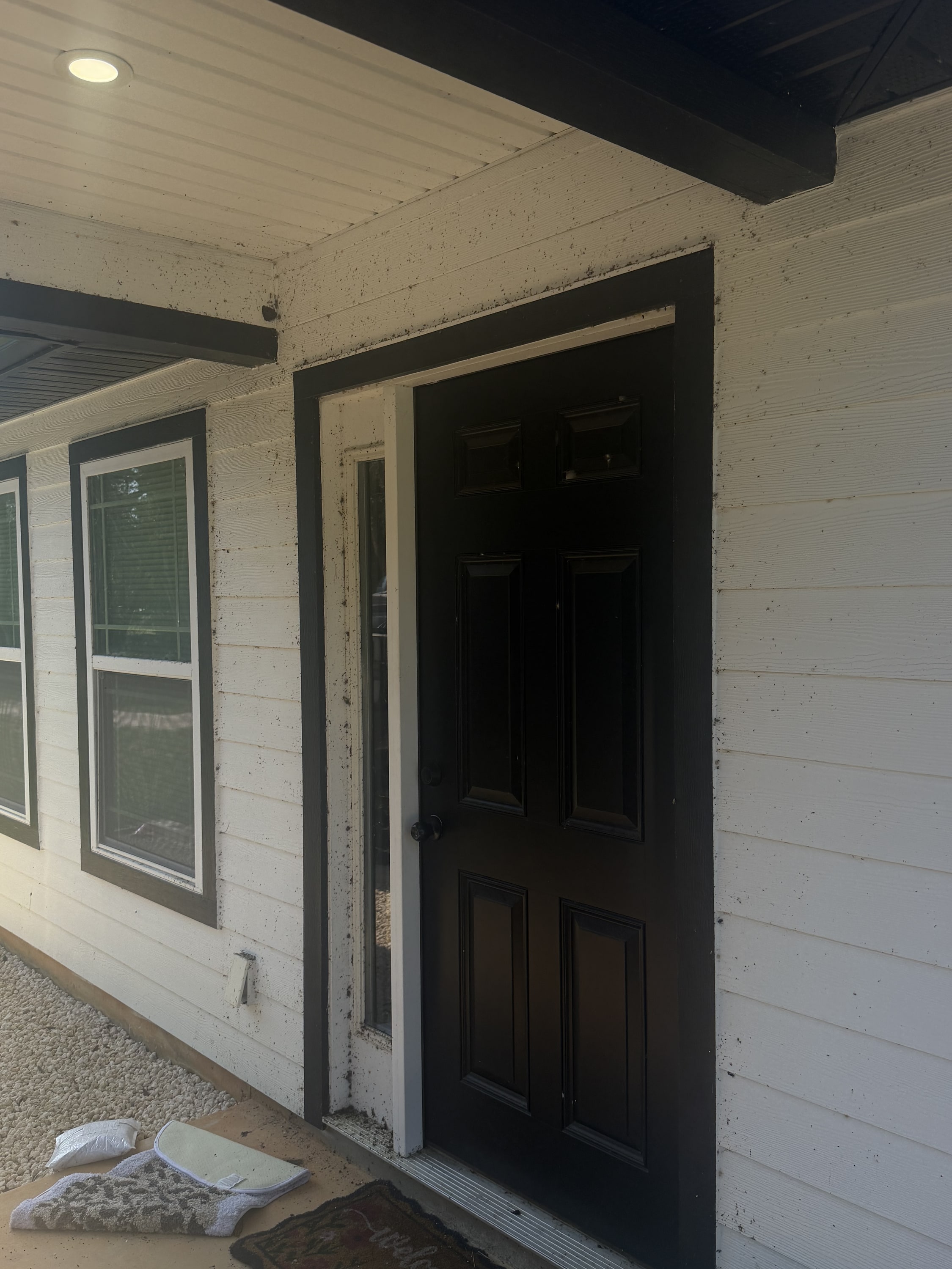 New black entrance door with white frame on rendered block wall with white windows.