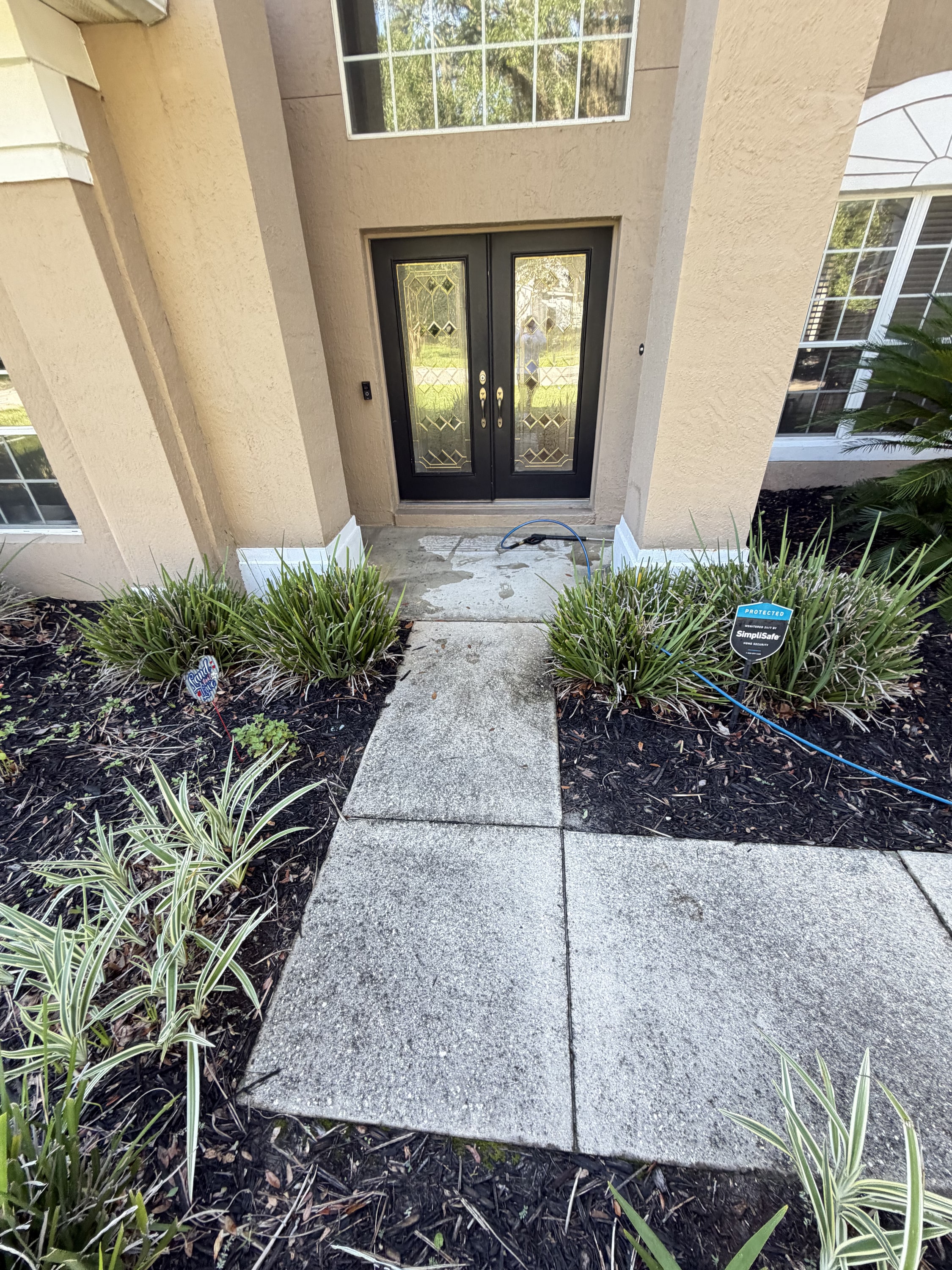 Front entrance with potted grasses flanking a concrete walkway to black double doors.