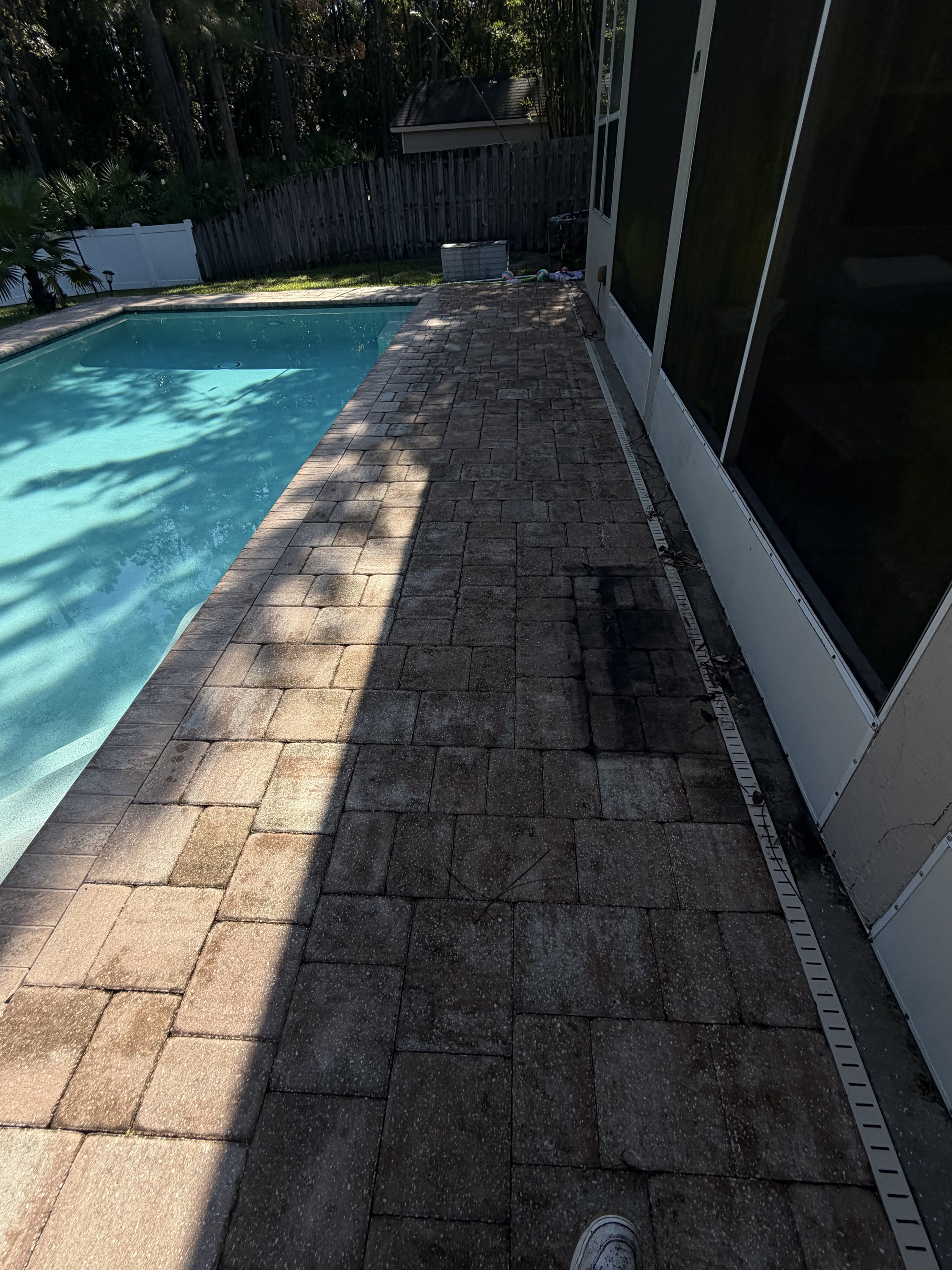 Block paver patio beside a swimming pool, half cleaned and half dirty, showing the contrast.
