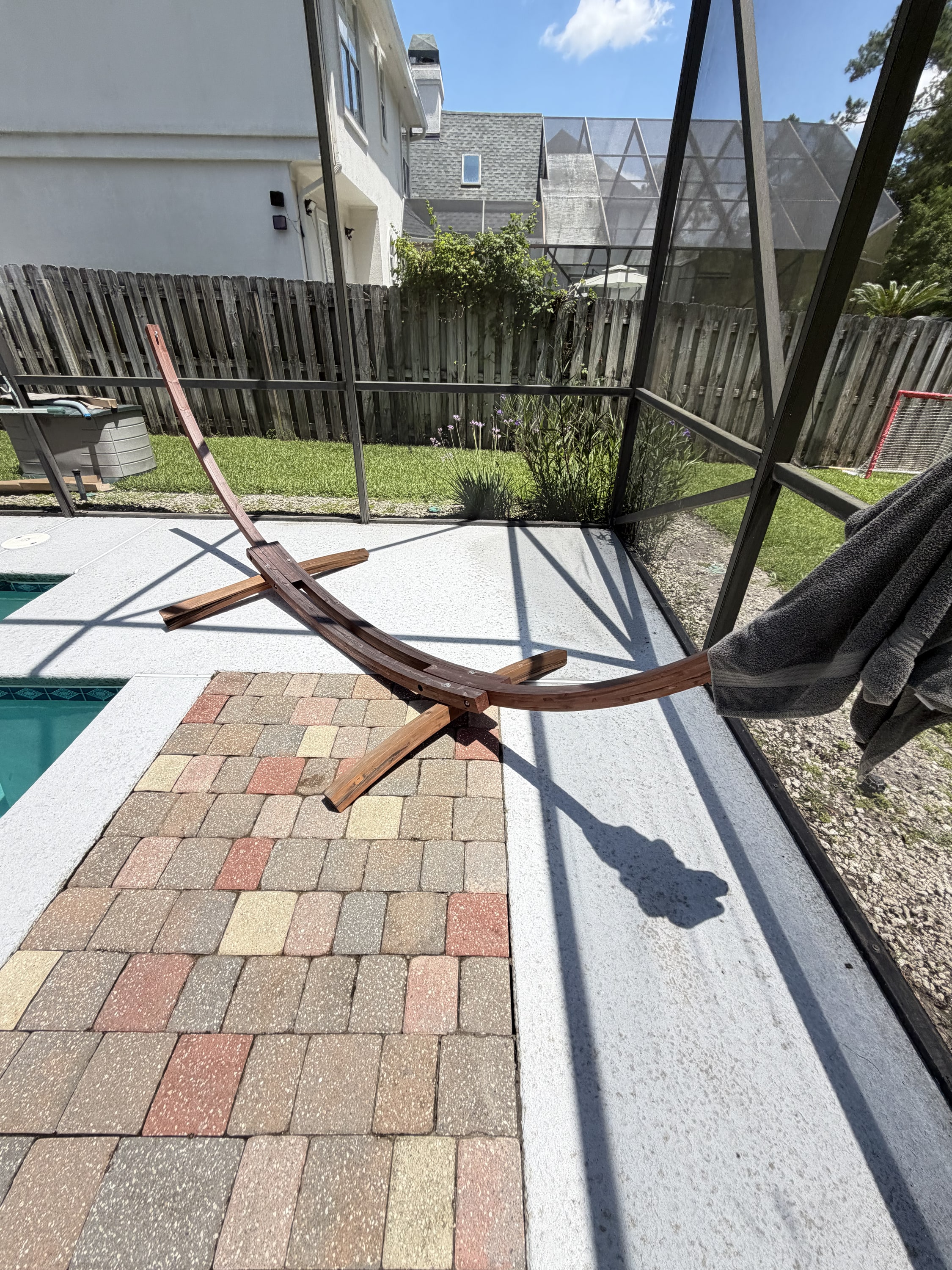 Interior view of screened pool enclosure with block paved patio and wooden fence beyond.
