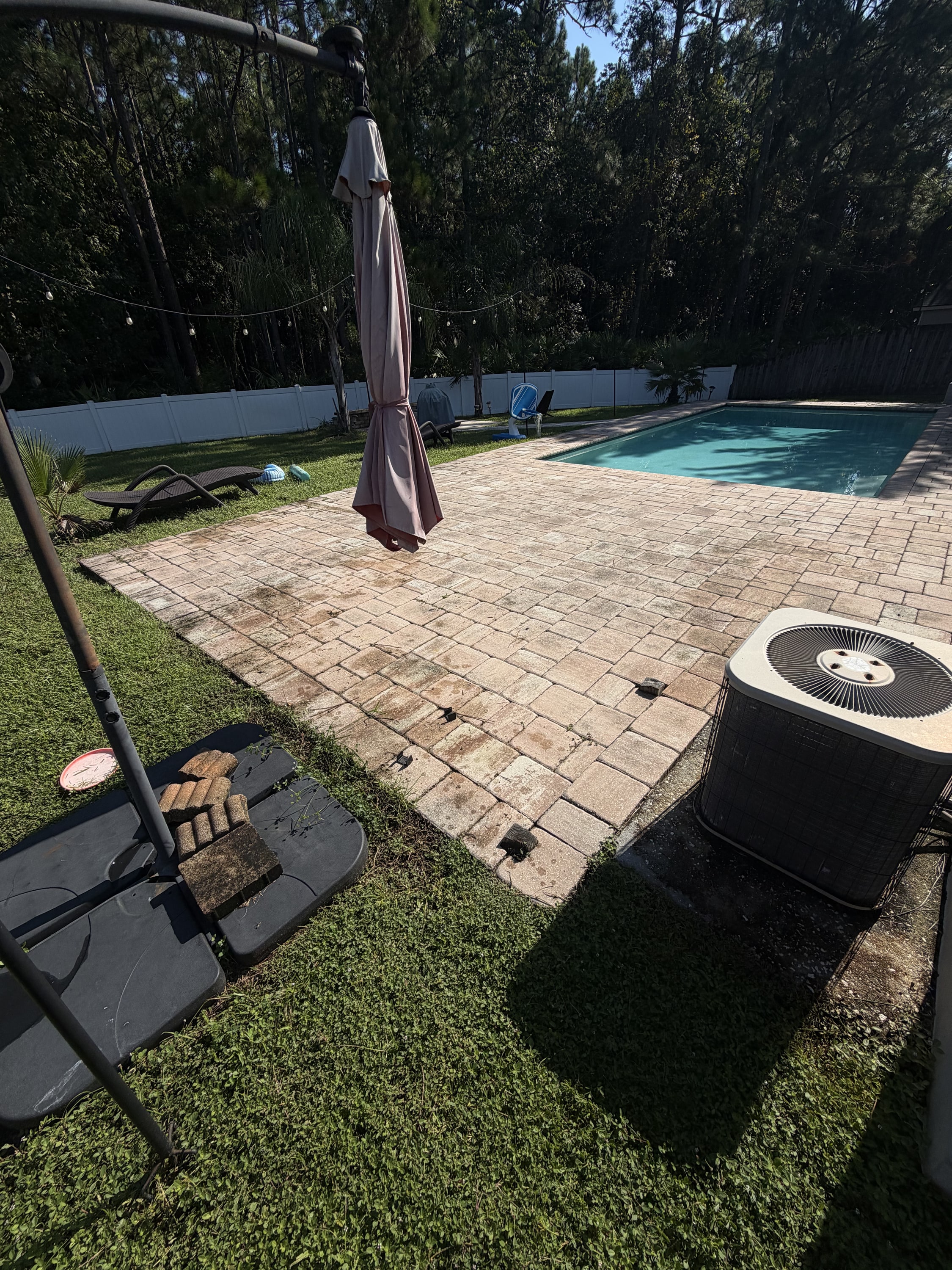 Newly installed block paved patio beside swimming pool with white fence and landscaping.