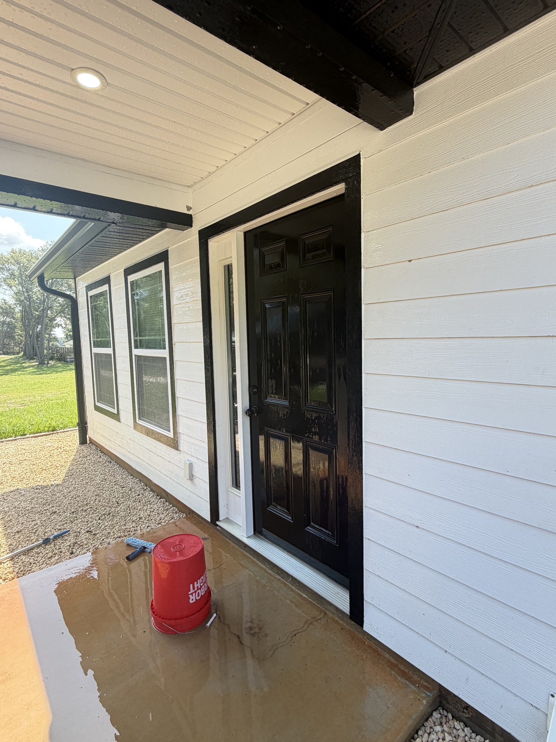White shiplap patio with black double doors and windows, wet concrete floor, gravel surround.