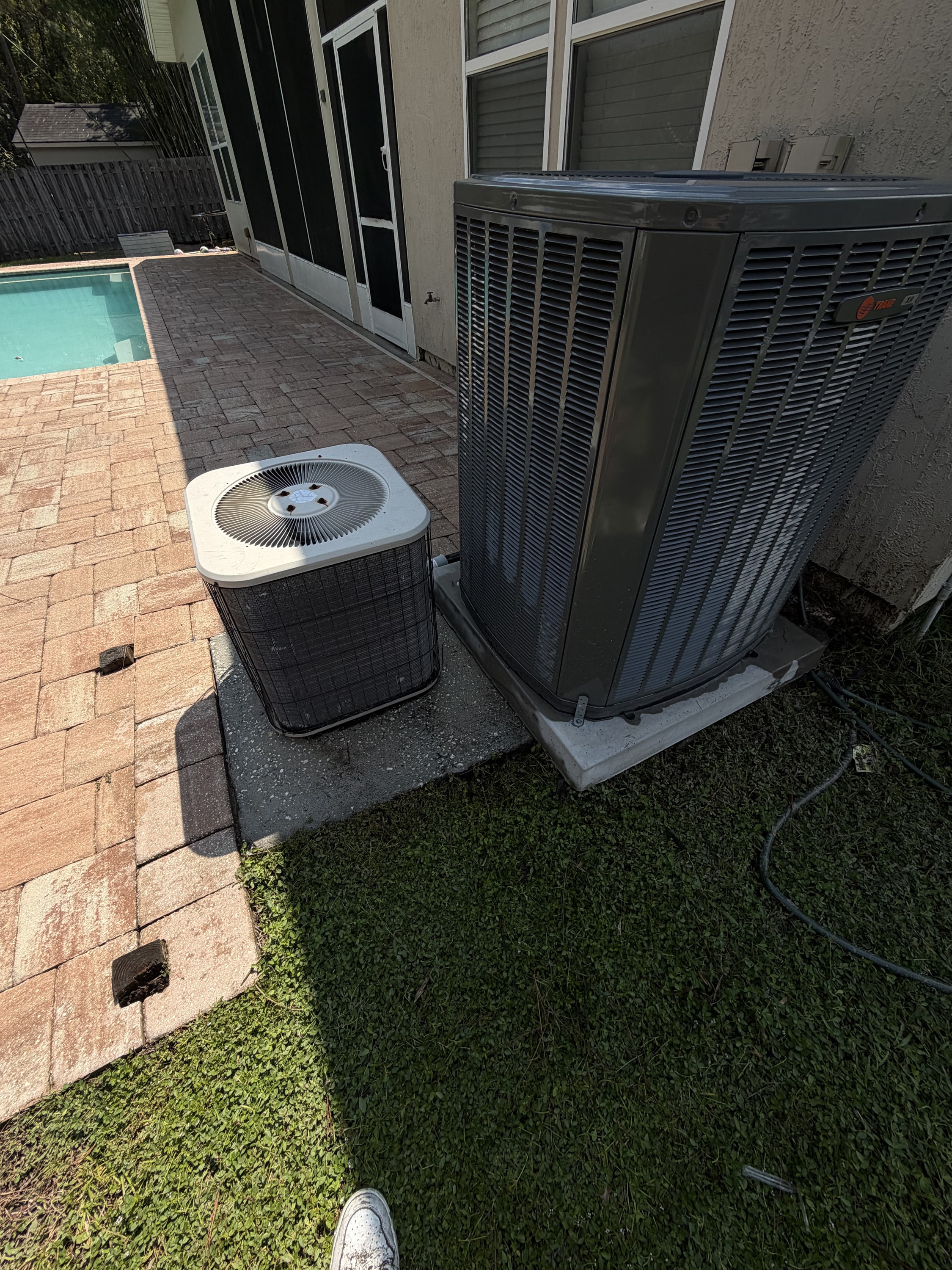 Two HVAC units side-by-side on concrete pads next to a residential pool area.