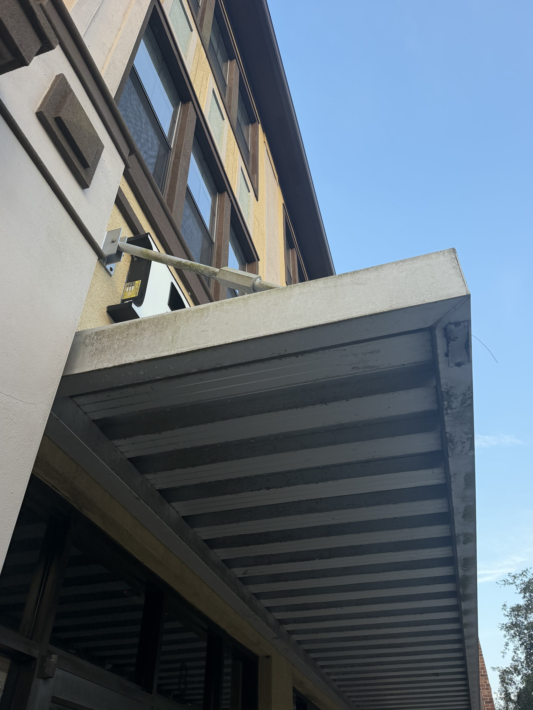 Modern louvered pergola attached to brick building, shot from below against blue sky.