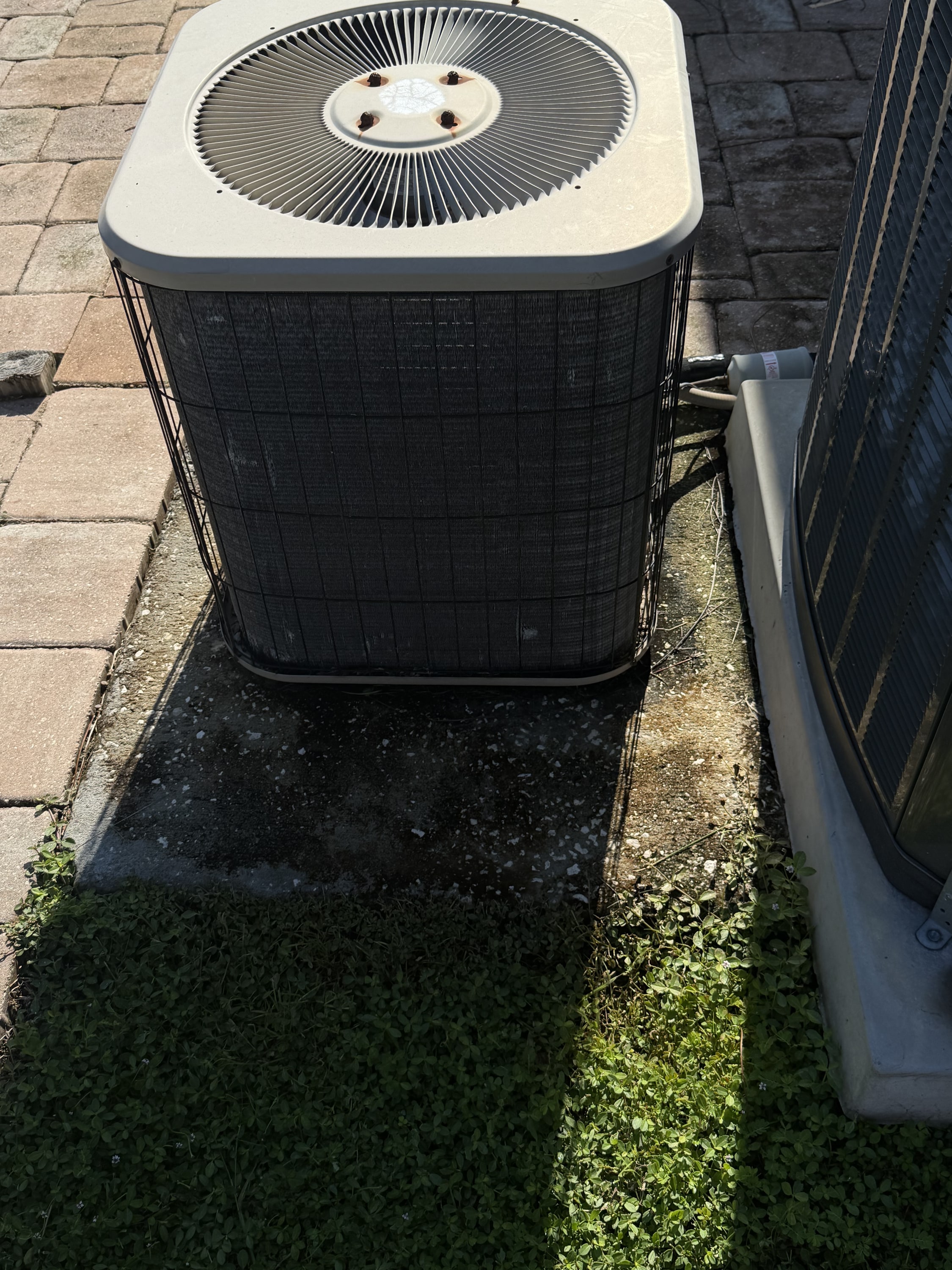 New AC unit installed on concrete pad with copper pipework, beside mossy ground.