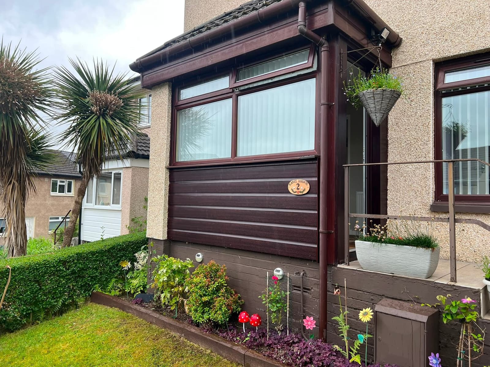 Brown garage conversion with large windows and door, rendered wall, canopy, and established garden borders with flowers.