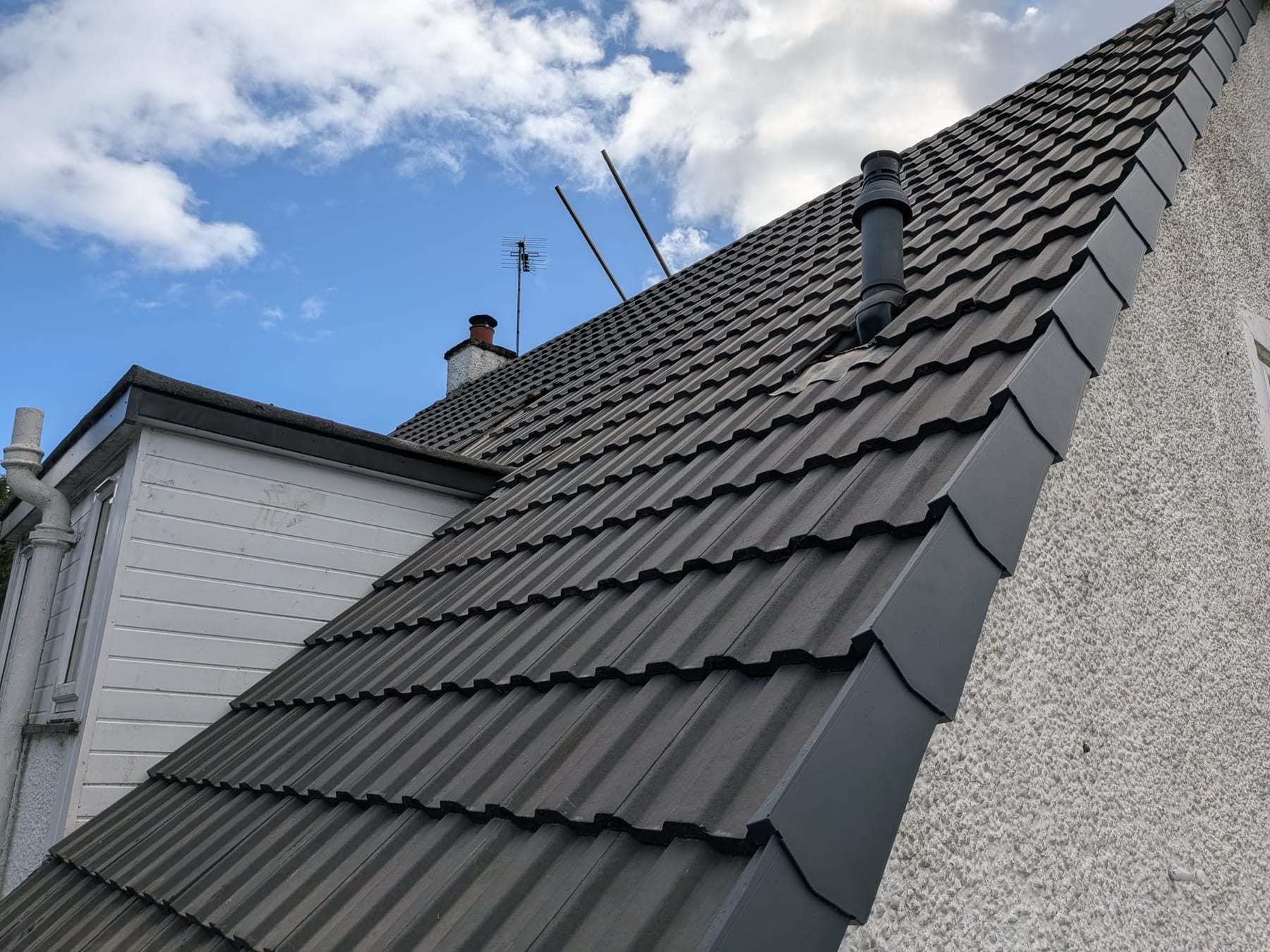 Grey interlocking roof tiles on pitched roof with flue pipe, chimney and clear sky
